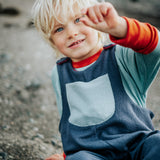 Child wearing a blue outfit with a pocket, sitting on a rocky surface.