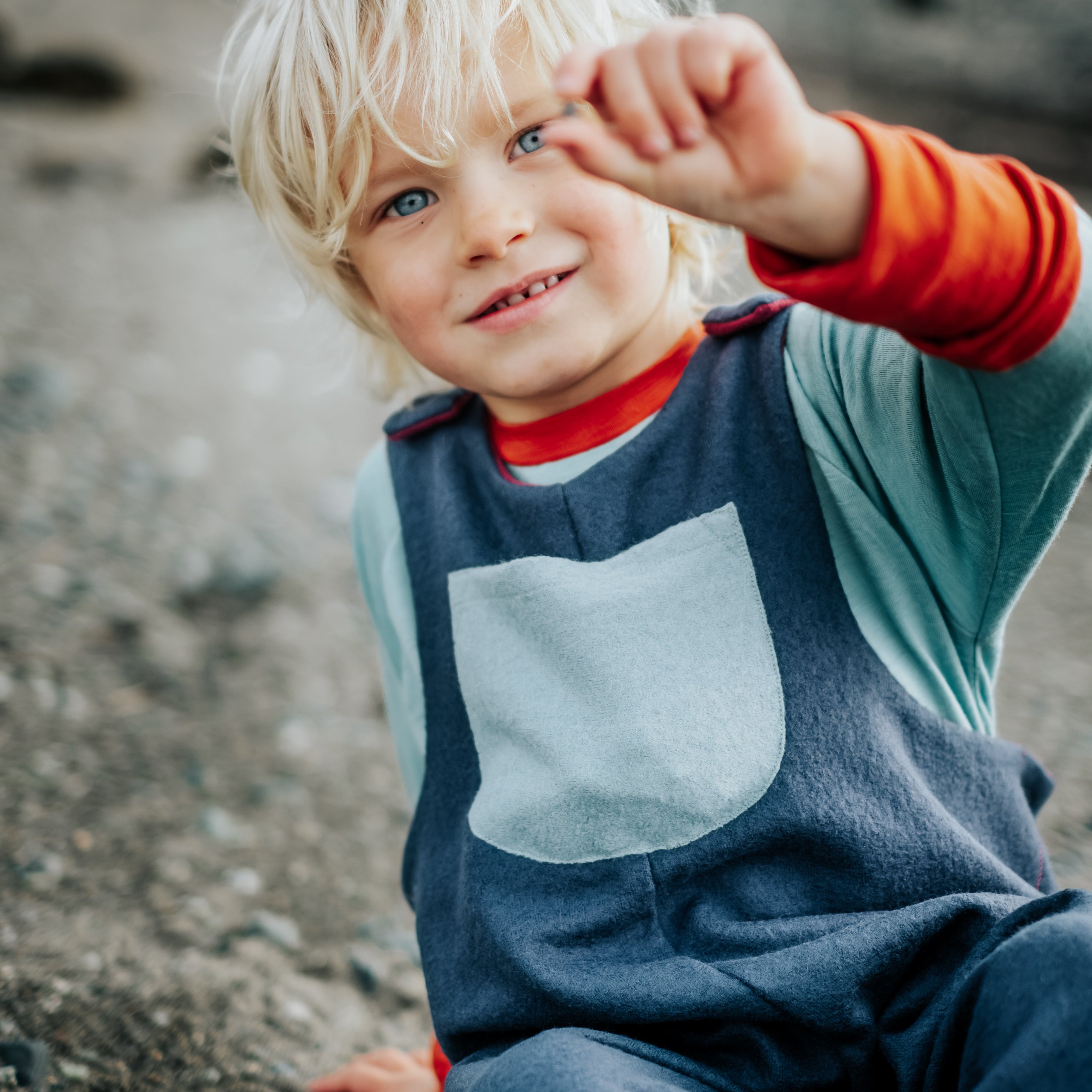 Child wearing a blue outfit with a pocket, sitting on a rocky surface.