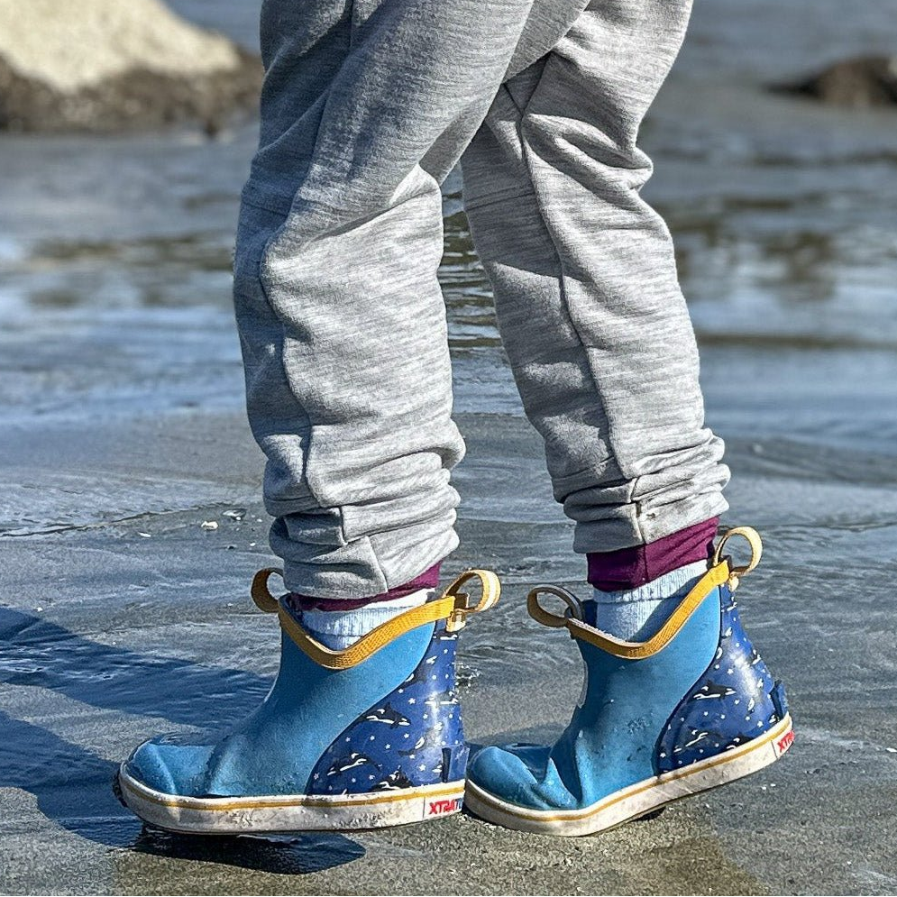 Blue rain boots with yellow accents worn by a person on a wet surface