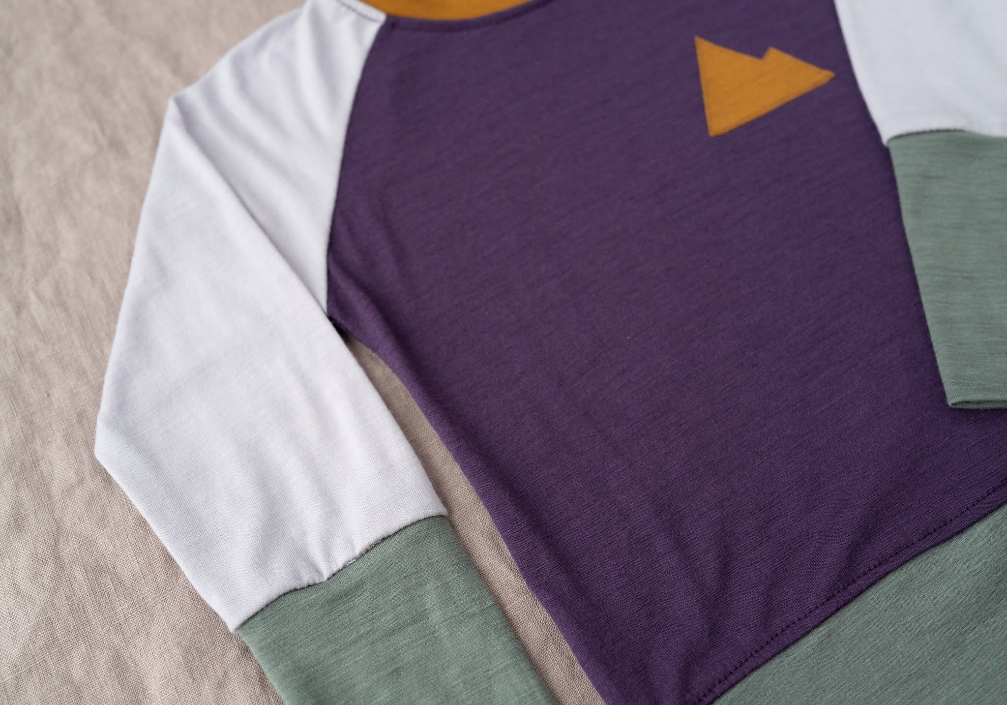 Color-blocked long-sleeve shirt with purple, white, green, and orange on a beige surface