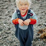Child wearing a blue and orange outfit standing on a rocky surface