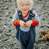 Child wearing a blue and orange outfit standing on a rocky surface