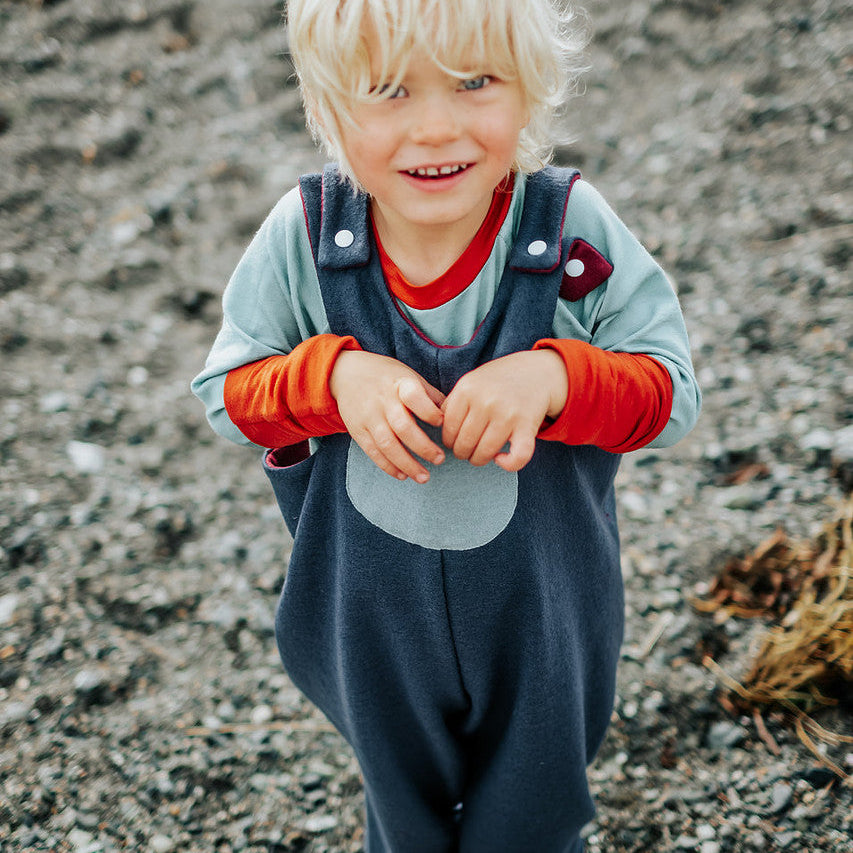 Child wearing a blue and orange outfit standing on a rocky surface