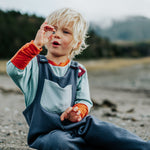 Child sitting on a rocky ground holding a small object, with a natural landscape in the background.