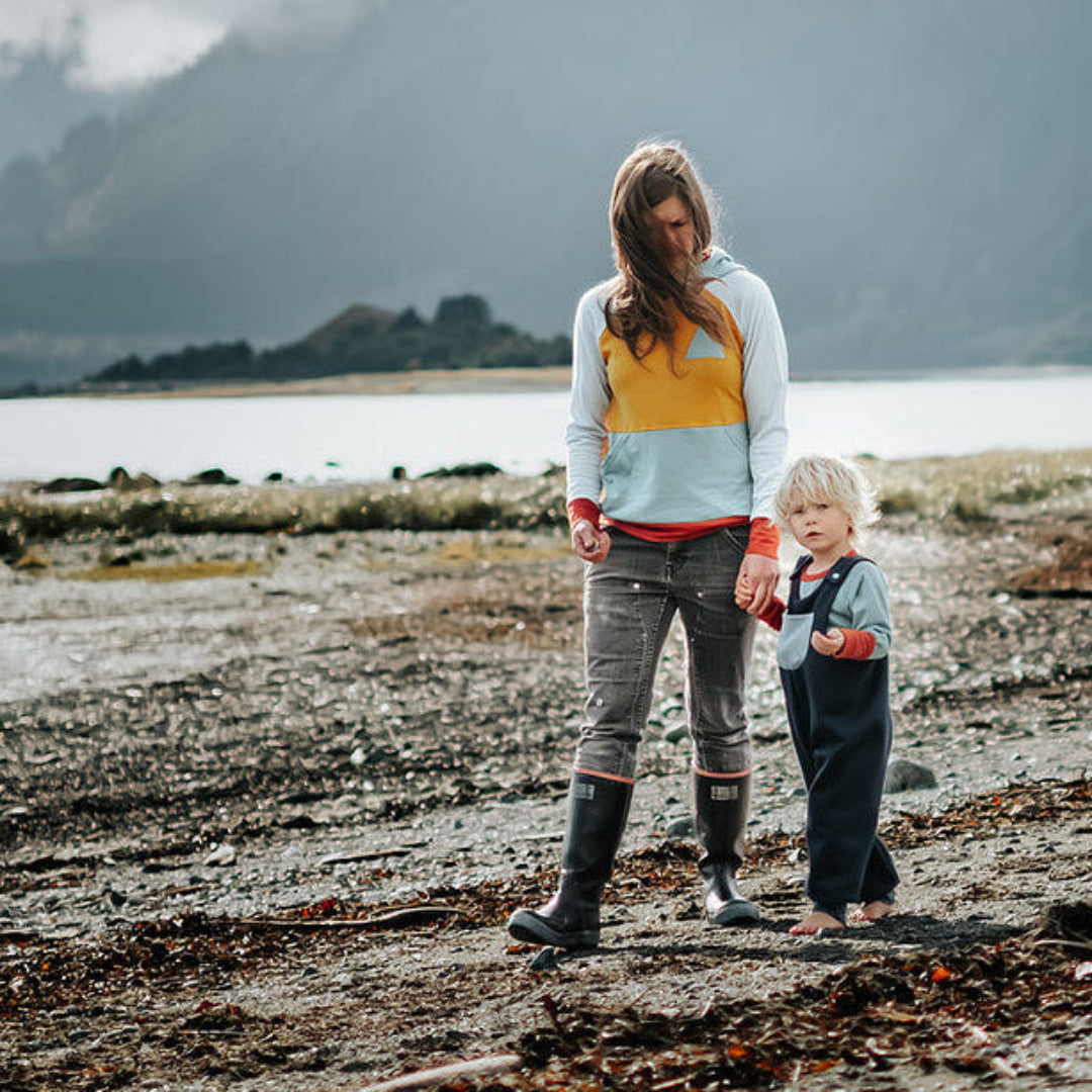Woman, child, and dog standing on a beach with mountains in the background