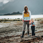 Woman, child, and dog standing on a beach with mountains in the background