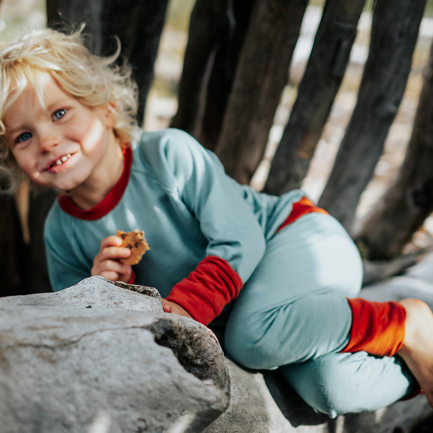 Child sitting on a rock in a natural setting in Essential Crew and Legging set in Birch Sky