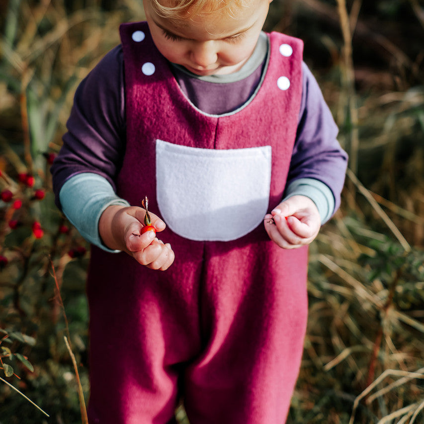 Child in a purple overalls with white buttons standing in a natural setting