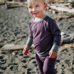 Child in purple merino base layers standing on a beach