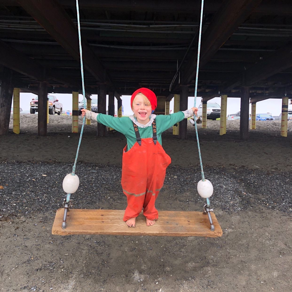 Kid in rain gear on swing under dock in kids grow with me merino wool base layers made in the usa by Wildhaven Wools